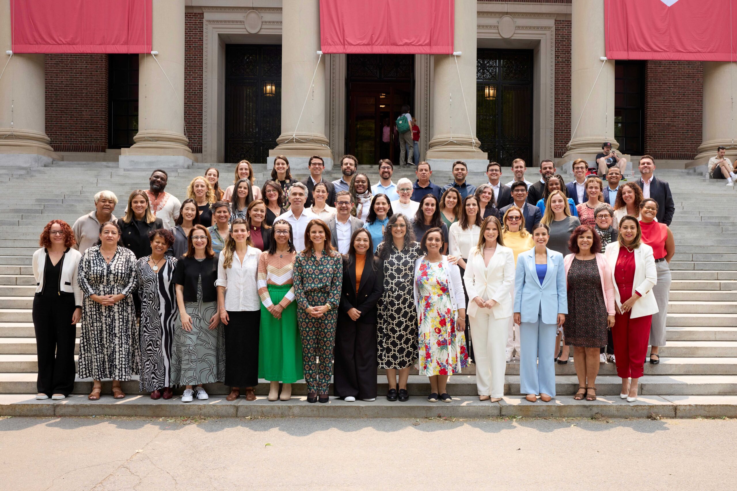 Grupo com cerca de 50 pessoas posicionadas em quatro filas, uma atrás da outra, na escadaria em frente à biblioteca da Universidade Harvard
