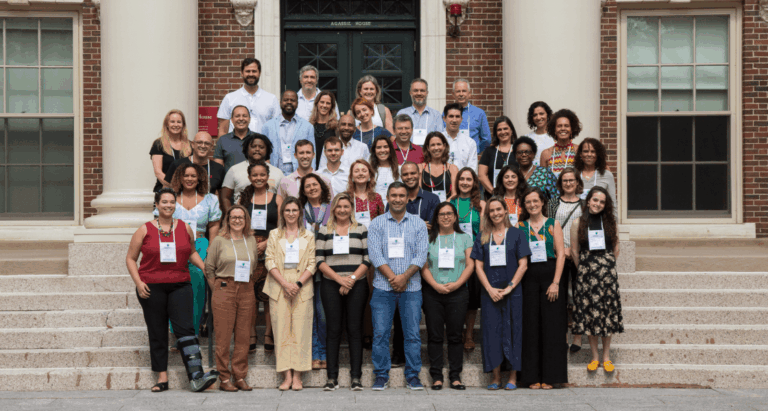 Grupo com cerca de 40 pessoas posicionadas em quatro filas, uma atrás da outra, na escadaria em frente à biblioteca da Universidade Harvard